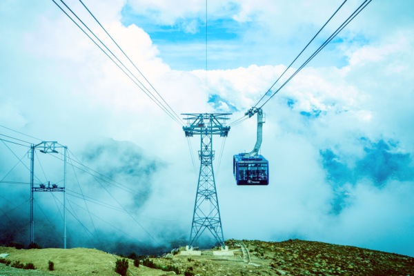 Mountain cable car gondola traveling through clouds on high alpine tramway cables above a misty landscape