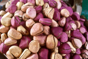 Pile of fresh purple and cream-colored kola nuts with natural brown markings, displayed in a market setting