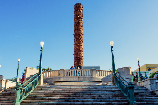 Puerto Rico GMS wide angle Plaza del Quinto Centenario Wide-angle view of the Plaza del Quinto Centenario in Old San Juan, Puerto Rico, featuring the prominent totem-like "Totem Telurico" sculpture, stone steps, green railings, and vintage-style street lamps under a clear blue sky