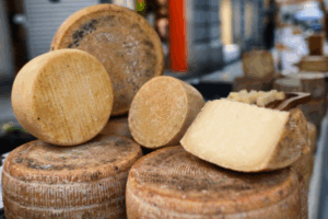 Stack of aged cheese wheels with a cut wedge and sample cubes displayed at an outdoor market stall