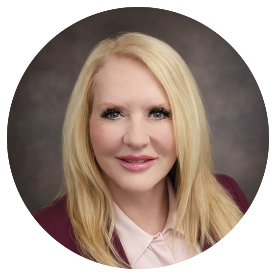 Professional headshot of a smiling blonde woman wearing a maroon blazer and light blouse against a neutral studio background