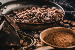 Roasted cacao beans in a metal pan with dark chocolate pieces and cocoa powder for artisanal chocolate making