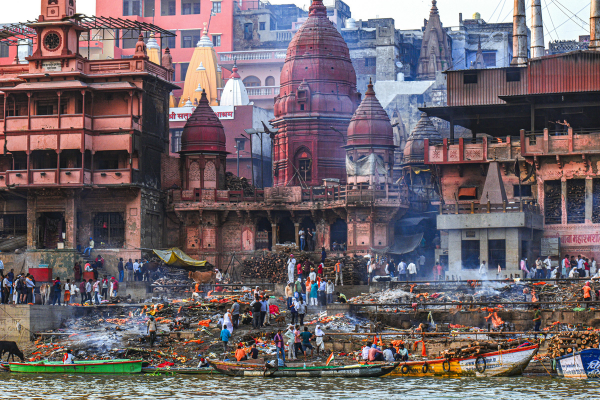 Riverside ghat with temples, boats, smoke and crowds gathered along the water in Varanasi, India