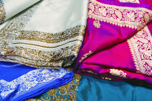 HFolded colorful silk fabrics with gold floral embroidery and ornate patterned borders in blue, teal, cream and magenta tones