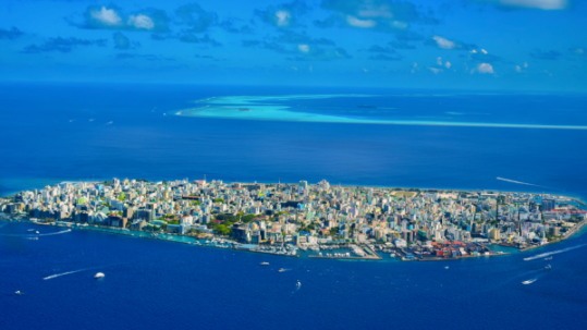 Aerial view of Malé city island in the Maldives surrounded by deep blue ocean, turquoise lagoon water and distant coral reef