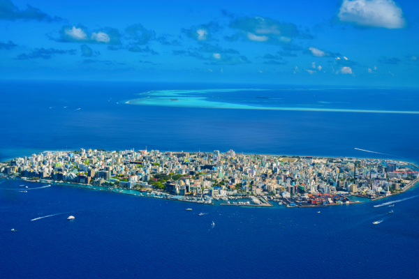 Aerial view of Malé city island in the Maldives surrounded by deep blue ocean, turquoise lagoon water and distant coral reef