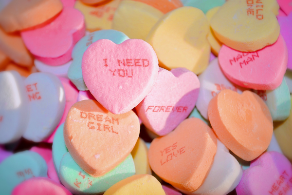 Heart-shaped Sweethearts candies in pastel colors are piled together with short messages printed on them
