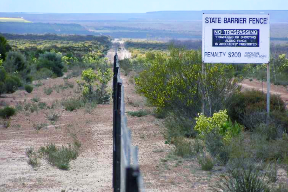 State Barrier Fence crossing dry scrubland with a no trespassing sign and distant hills on the horizon