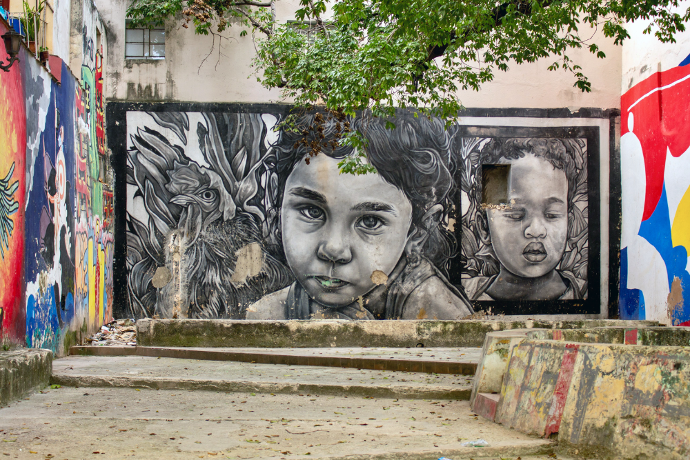 Urban street mural depicting children's faces on a vibrant alleyway wall
