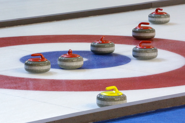 Curling stones with red and yellow handles positioned on the target circles of an indoor ice sheet