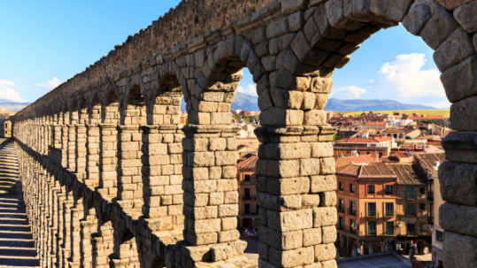 View along an ancient stone aqueduct with repeating arches overlooking a historic city and surrounding landscape