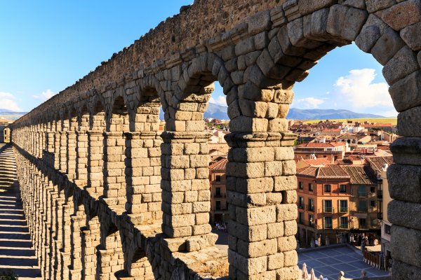 View along an ancient stone aqueduct with repeating arches overlooking a historic city and surrounding landscape