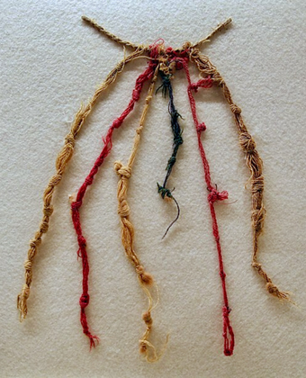 Close-up of several braided and twisted cords in red, tan, and dark blue, each tied with multiple knots and connected at one end, displayed on a light-colored background