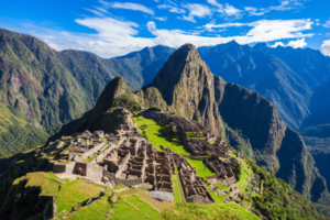 Panoramic view of Machu Picchu with its stone ruins set among steep green mountain peaks under a bright blue sky