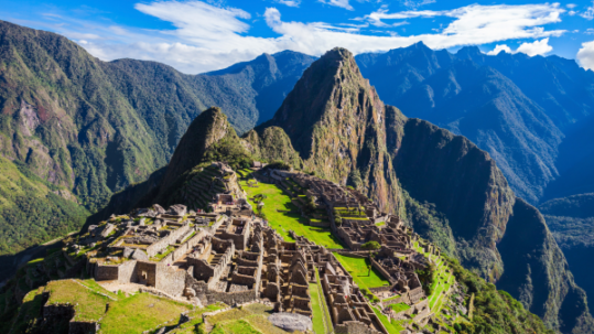 Panoramic view of Machu Picchu with its stone ruins set among steep green mountain peaks under a bright blue sky