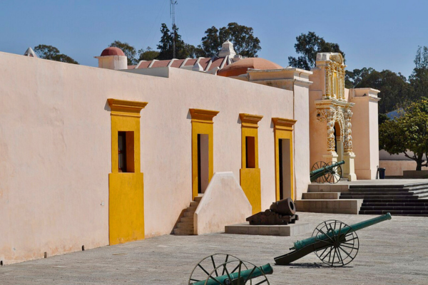 Courtyard of a historic fort with pastel-colored buildings, decorative architectural details, and several cannons displayed on wheeled carriages