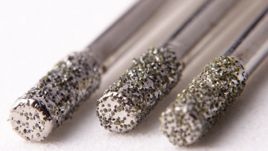 Close-up of three cylindrical metal tools with coarse, diamond-coated abrasive tips arranged side by side on a white background