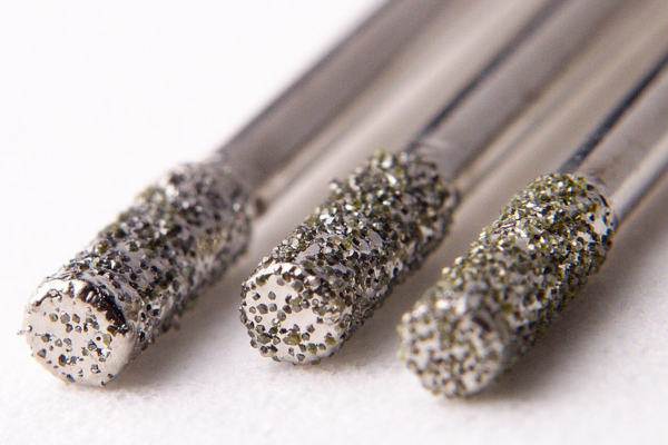 Close-up of three cylindrical metal tools with coarse, diamond-coated abrasive tips arranged side by side on a white background