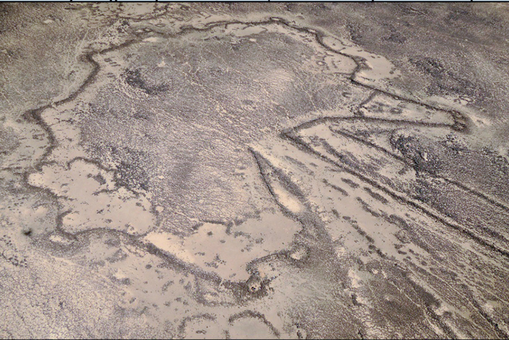 Aerial view of a large geoglyph outlined with stones across a barren desert plain