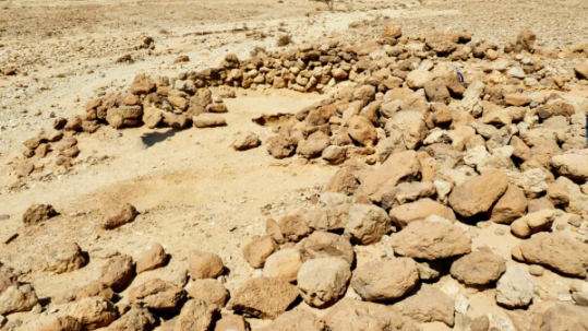 Circular stone structure built from stacked rocks in a rocky desert landscape with rugged mountains in the background
