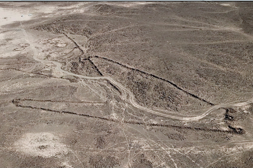 Aerial view of long linear stone alignments and geometric rock features crossing a barren desert landscape