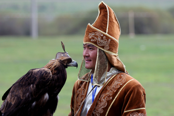 Kazakh eagle hunter in ornate traditional clothing standing beside a large golden eagle used in the ancient practice of falconry