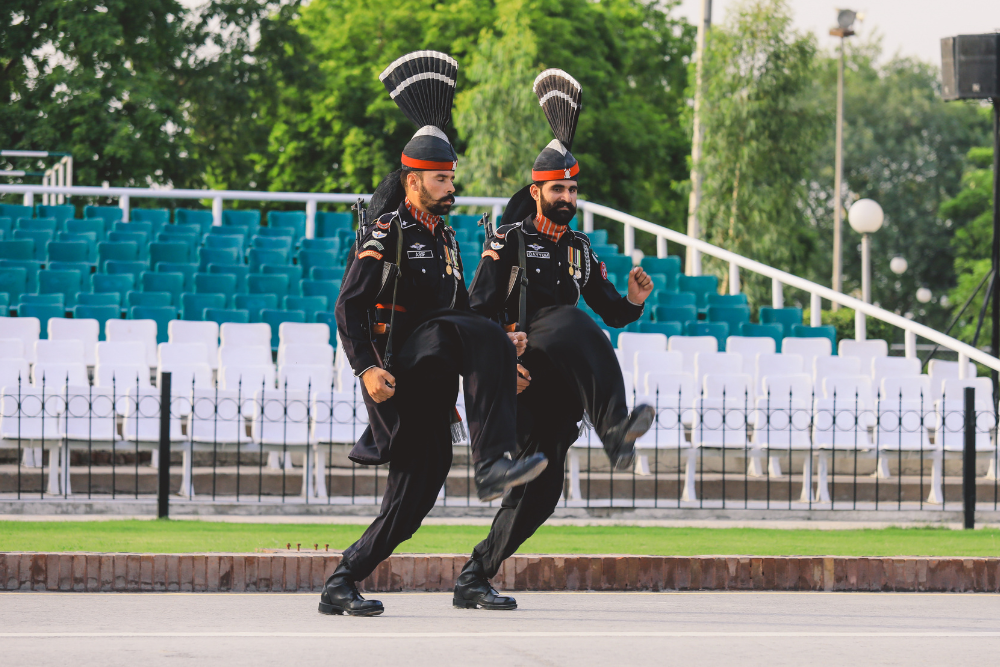 Rangers de Pakistán con uniformes ceremoniales negros y tocados en forma de abanico realizan una marcha sincronizada de pasos altos en la ceremonia fronteriza de Wagah