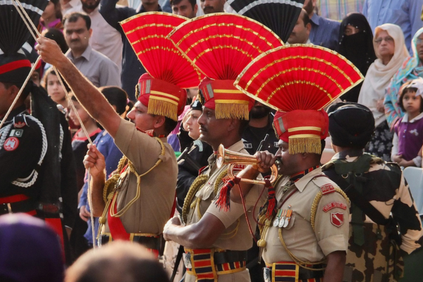 Indian border security personnel wearing ceremonial uniforms with red fan-shaped headdresses perform in the Wagah border ceremony as a crowd watches from the stands