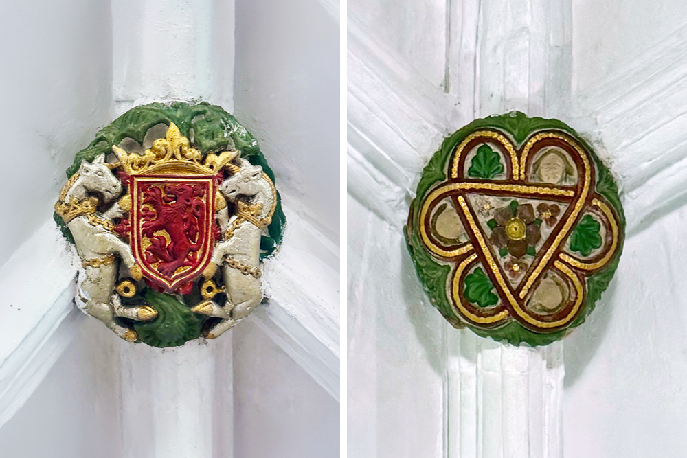 Two decorative Gothic ceiling bosses feature a crowned red lion shield flanked by unicorns on the left and an ornate interlaced floral emblem in red, green, and gold on the right.