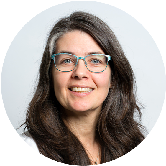 Professional headshot of a smiling woman with long dark brown hair and teal glasses against a light gray background