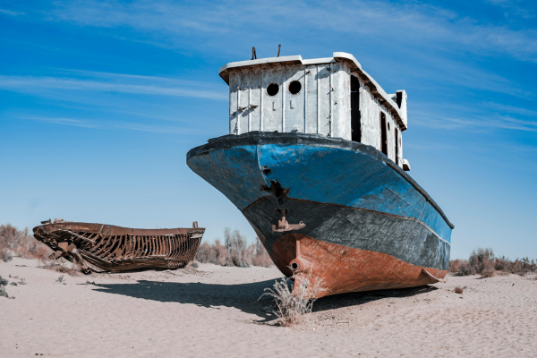 Abandoned blue-and-white fishing boat and decaying wooden hull resting on the sandy former seabed of the Aral Sea