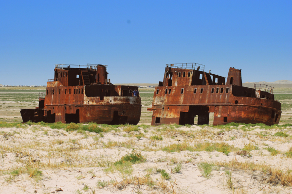 Two rusting abandoned shipwrecks stranded on the dry former seabed of the Aral Sea under a clear blue sky