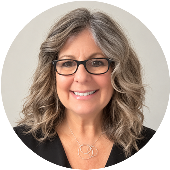 Professional headshot of a smiling woman with shoulder-length wavy gray hair, black glasses, and a silver necklace against a neutral background