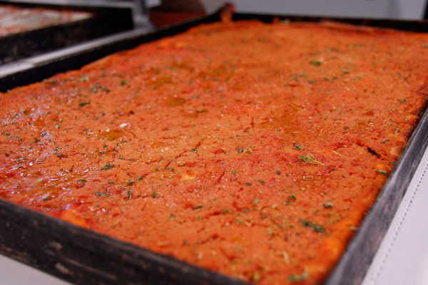 Traditional Rhode Island pizza strips topped with tomato sauce and herbs, baked in a large rectangular black metal pan