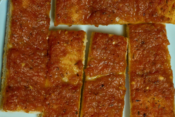 Rectangular Rhode Island pizza strips topped with seasoned tomato sauce, cut into individual pieces and arranged on a white serving tray